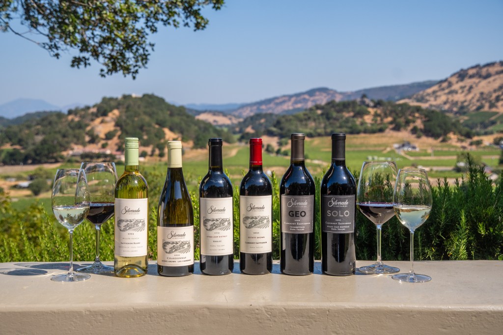 6 silverado wine bottles on ledge with wine glasses in front of a vineyard