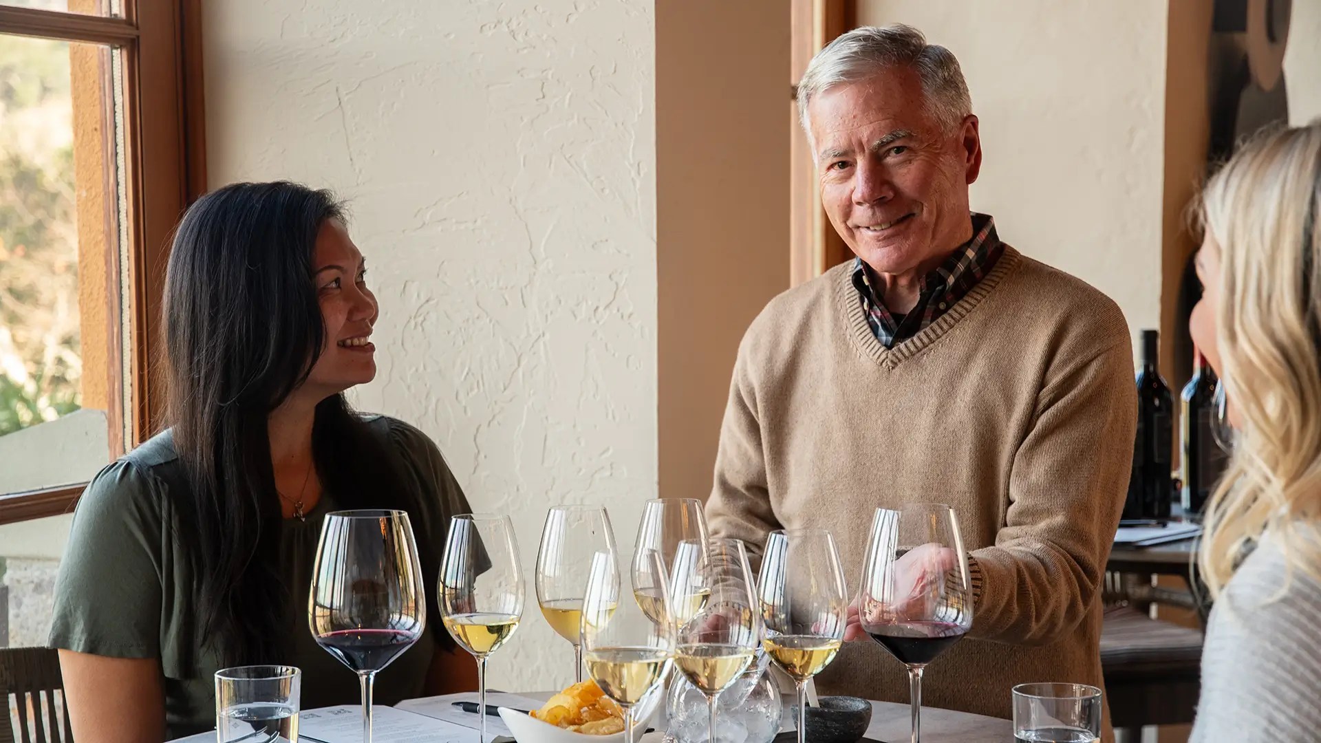 Wine tasting host speaking with guests around a table of red and white wines